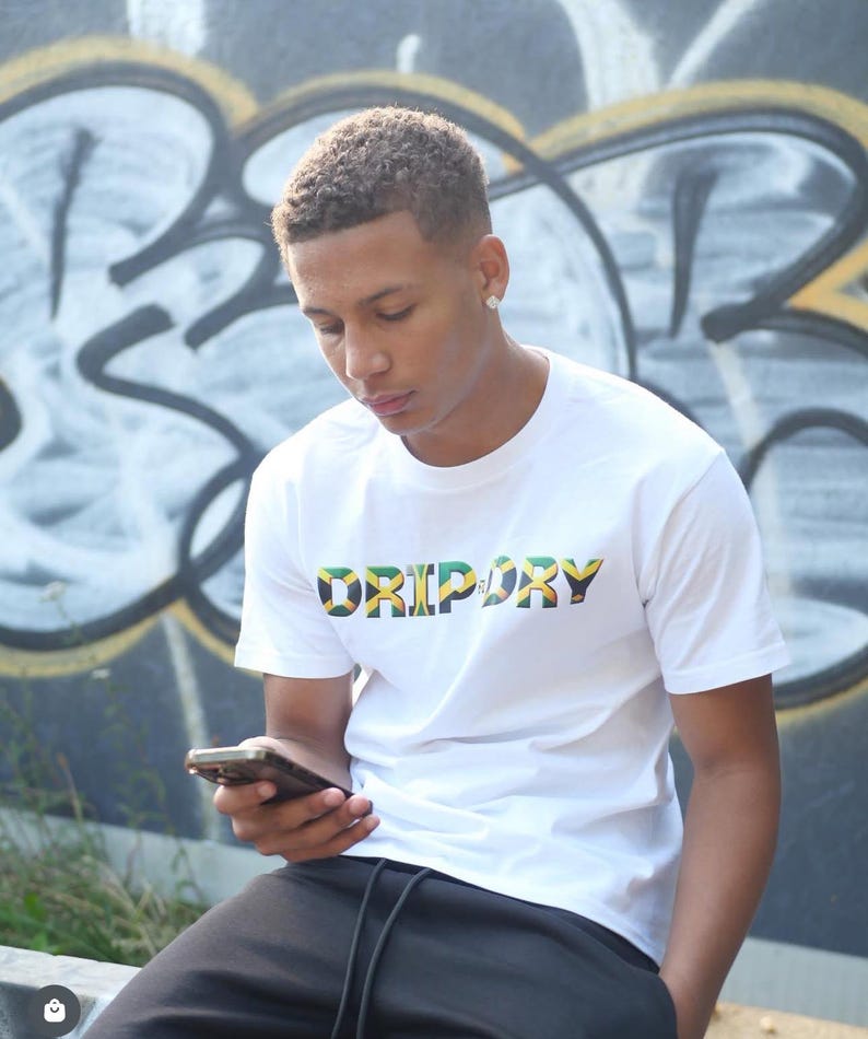 May include: A white t-shirt with the word "DRIPORY" printed in green, yellow, and black letters. The letters are outlined in black and have a Jamaican flag design.