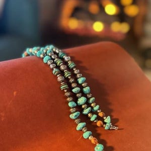 Puede incluir: Un collar de cuentas turquesa y plata con detalles marrones. El collar está hecho de múltiples hileras de cuentas y tiene un cierre de plata.