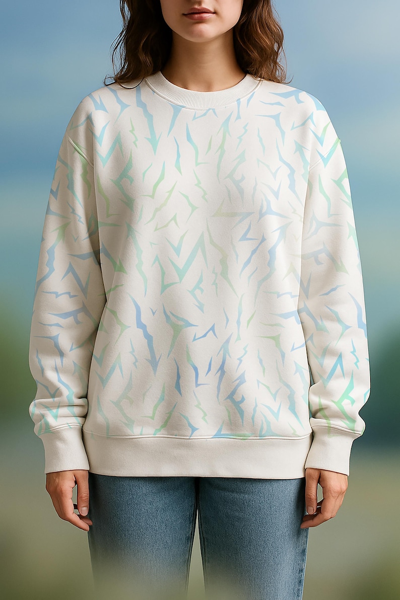 May include: Cream-coloured sweatshirt featuring a repeating pattern of blue and green abstract shapes. The long-sleeved top has a crew neck and ribbed cuffs and hem. The model is wearing blue jeans.