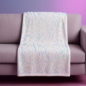 May include: A white throw blanket with a pattern of blue and green abstract shapes, draped over a grey sofa. The background gradient transitions from purple to pink.