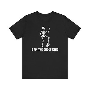 Può includere: T-shirt nero con grafica di uno scheletro bianco. Lo scheletro è in piedi su una gamba e alza una mano. Il testo "I AM THE GHOST KING" è stampato sotto.