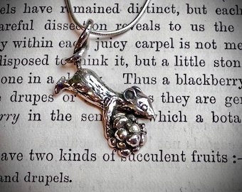 May include: A silver-toned metal pendant shaped like a small mouse holding a textured, round object. The mouse is suspended from a thin, metallic snake chain. The pendant features a polished finish with visible details on the mouse's body.