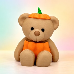 Può includere: Una statuetta di orsacchiotto marrone chiaro con un cappello a forma di zucca arancione brillante sulla testa e una sezione del corpo abbinata a forma di zucca arancione. L'orso ha occhi neri circolari, naso marrone e finitura opaca.