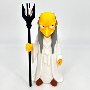 May include: A yellow-skinned character figurine with a pointed nose, thin grey hair, and a white robe. The figure holds a tall black staff topped with a white sphere. The character has a stern expression, brown shoes, and is standing upright.