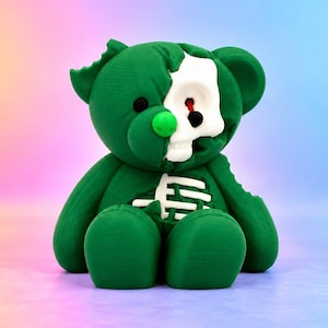 Può includere: Una statuetta di orsacchiotto verde scuro con un teschio bianco parzialmente esposto sul lato sinistro del viso e una gabbia toracica bianca visibile sul petto. L'orso ha un naso verde brillante, occhi neri e una finitura superficiale testurizzata.