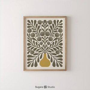May include: A framed art print featuring a stylized floral design. The artwork showcases a mustard-yellow vase holding olive-green leaves and flower-like shapes against a cream background. The print is enclosed in a light-brown wooden frame.