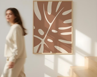 May include: A framed art print featuring a large, stylized monstera leaf in shades of brown and cream. The artwork is displayed on a white wall, with a wooden frame. The Sugara Studio logo is visible in the bottom right corner. The overall theme is modern and minimalist.