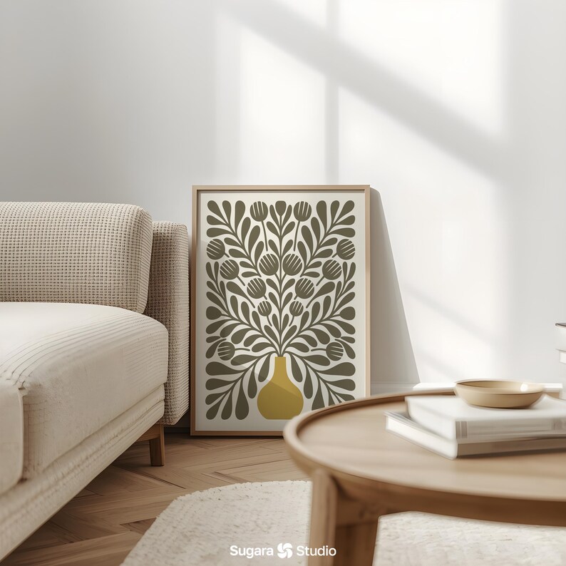 May include: A framed art print featuring a stylized floral design. The artwork showcases a yellow vase filled with olive-green leaves and flower-like shapes against a cream background. The print is displayed in a light-colored wooden frame, adding a touch of natural warmth to the decor.