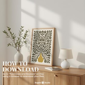 May include: A framed art print featuring a floral design in olive green and yellow, displayed on a wooden cabinet. A white vase with greenery and a small lamp are also on the cabinet. Text on the image reads "HOW TO DOWNLOAD".