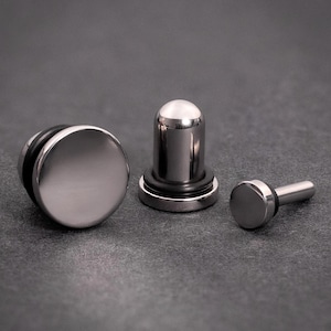 Puede incluir: Tres expansores de oreja plateados, uno con la parte superior redondeada y dos con la parte superior circular plana.