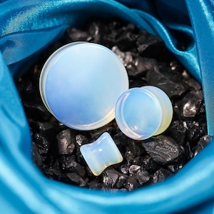 Könnte beinhalten: Drei Ohrstecker aus Opalit in verschiedenen Größen. Der größte Stecker ist eine runde Scheibe, der mittlere Stecker ist eine runde Scheibe und der kleinste Stecker ist tropfenförmig. Die Stecker befinden sich auf einem schwarzen Hintergrund.