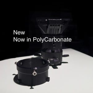 Puede incluir: Un adaptador de lente de cámara negro hecho de policarbonato. El adaptador tiene un anillo roscado y una base plana. El texto "New Now in Polycarbonate" es visible en la imagen.
