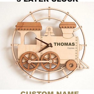 Puede incluir: Un reloj de madera de 3 capas con forma de tren, con el texto "THOMAS Express" en el lateral. Las manecillas del reloj son de color marrón oscuro. El reloj está rodeado por un marco circular. El texto "3 LAYER CLOCK" y "CUSTOM NAME" están arriba y abajo.