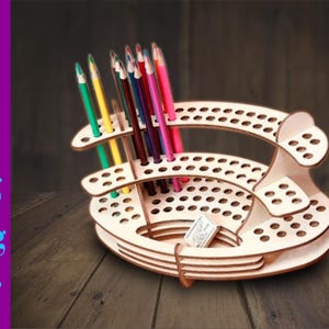 Könnte beinhalten: Ein Bleistifthalter aus Holz mit mehreren Ebenen und Löchern zum Aufbewahren von Bleistiften. Der Halter ist aus hellbraunem Holz und hat eine runde Basis. Es befinden sich farbige Bleistifte im Halter.