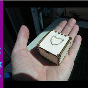 Puede incluir: Una pequeña caja de madera con un diseño de corazón en la tapa. La caja es de color marrón claro y tiene un acabado de madera natural.