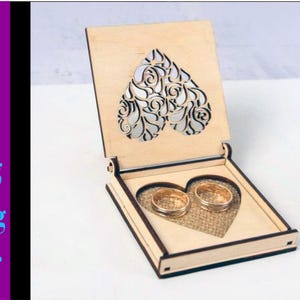 May include: A wooden ring box with a heart-shaped cutout and two gold rings inside. The box is made of light wood and has a natural finish.