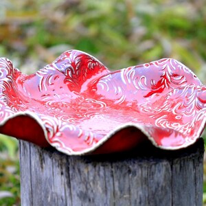 Może przedstawiać: Czerwona ceramiczna miska z białym wzorem kwiatowym. Miska ma falisty brzeg i stoi na pniu drzewa.