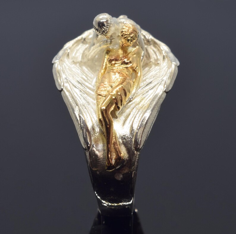 A close-up image of a ring featuring a gold-toned figure of a woman with a winged design.