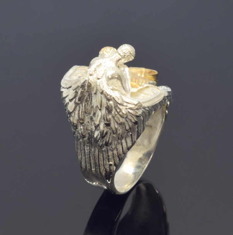 A silver ring with a detailed design of a winged figure, possibly a deity or angel, on the back.