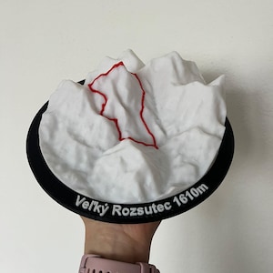 Könnte beinhalten: Ein 3D-gedrucktes topografisches Modell des Berges Velky Rozsutec, mit einem weißen Gipfel mit roter Kontur, auf einer schwarzen kreisförmigen Basis. Der Text "Velky Rozsutec 1610m" ist auf der Basis aufgedruckt.