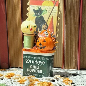 Boîte à épices vintage Durkee Chili Powder décorée d'articles de fête d'Halloween avec une tête de mort vintage et une citrouille d'Halloween, avec une carte de voeux de chat noir.