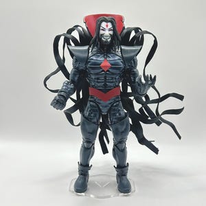 May include: A black and red action figure of a superhero with a long black cape and a red diamond on his chest. The figure is standing on a clear plastic base.