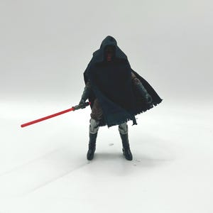 May include: A Star Wars action figure of Darth Maul, a Sith Lord, stands with a red lightsaber. The figure is wearing a black hooded cloak and black boots. The figure has a red face and is posed against a white background.