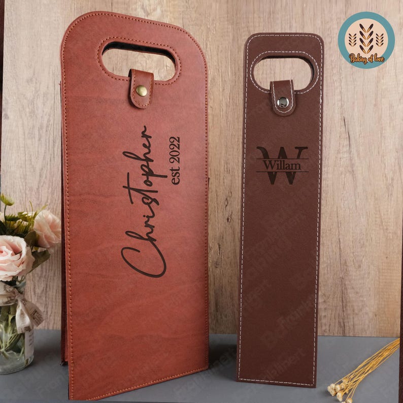 K&ouml;nnte beinhalten: Zwei braune Weinflaschentaschen aus Leder mit personalisierten Gravuren. Eine Tasche tr&auml;gt den Namen "Christopher" und das Datum "EST 2022" eingraviert. Die andere Tasche tr&auml;gt das Initial "W" und den Namen "William" eingraviert.