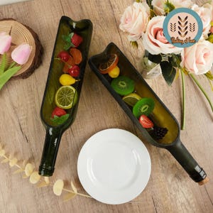 Peut inclure: Deux bouteilles de vin en verre vert transformées en plats de service. Les bouteilles sont remplies de fruits, notamment des fraises, des kiwis, des citrons et des limes. Les bouteilles sont posées sur une surface en bois avec une assiette blanche et des fleurs roses en arrière-plan. Le texte "Baking of Love" est visible dans le coin supérieur droit de l'image.