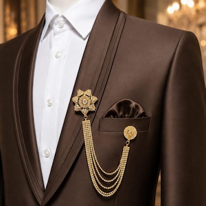 Peut inclure: Une veste de costume marron foncé avec une chemise blanche à col et une pochette marron assortie. Une broche dorée en forme d'étoile avec des pierres claires est fixée au revers, reliée par quatre chaînes drapées à une épingle circulaire.