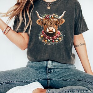 Pu&ograve; includere: T-shirt grigio scuro con grafica di una mucca delle Highlands. La mucca &egrave; adornata con una ghirlanda e una sciarpa festive, perfette per le festivit&agrave; natalizie. La maglietta &egrave; realizzata in un materiale morbido ed &egrave; adatta per un abbigliamento casual.