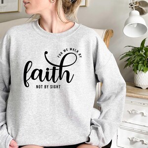 Puede incluir: Una sudadera gris con el texto "For we walk by faith not by sight" impreso en negro.