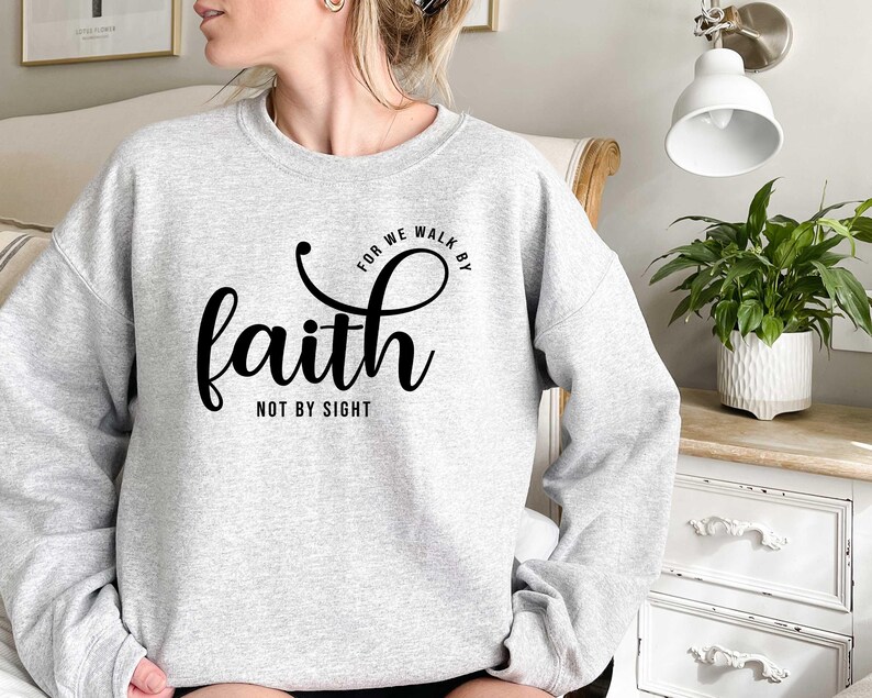 Puede incluir: Una sudadera gris con el texto "For we walk by faith not by sight" impreso en negro.