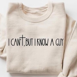 May include: A cream-colored sweatshirt with the text "I CAN'T, BUT I KNOW A GUY" printed in black. The word "CAN'T" has a cross symbol replacing the apostrophe. The sweatshirt is folded neatly.
