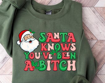 May include: Green sweatshirt with the text "SANTA KNOWS YOU'VE BEEN A BITCH" in red, green, and pink. The design includes a cartoon Santa Claus with a white beard and red hat. Holly accents are incorporated into the text.