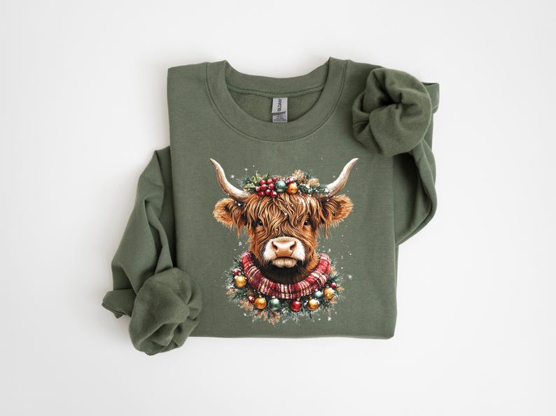 Pu&ograve; includere: Felpa verde oliva con un'illustrazione ad acquerello di una mucca delle Highlands decorata per le feste. La mucca ha una ghirlanda festosa e una sciarpa a quadri. Il disegno &egrave; centrato sulla parte anteriore del top a maniche lunghe.
