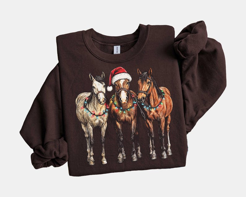 May include: A dark brown sweatshirt featuring a graphic of three horses adorned with Christmas lights. The center horse wears a Santa hat. The horses are in a row, with a white, brown, and chestnut horse.