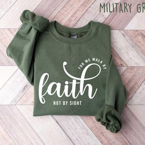 Puede incluir: Una sudadera verde con el texto "For we walk by faith not by sight" en letras blancas.