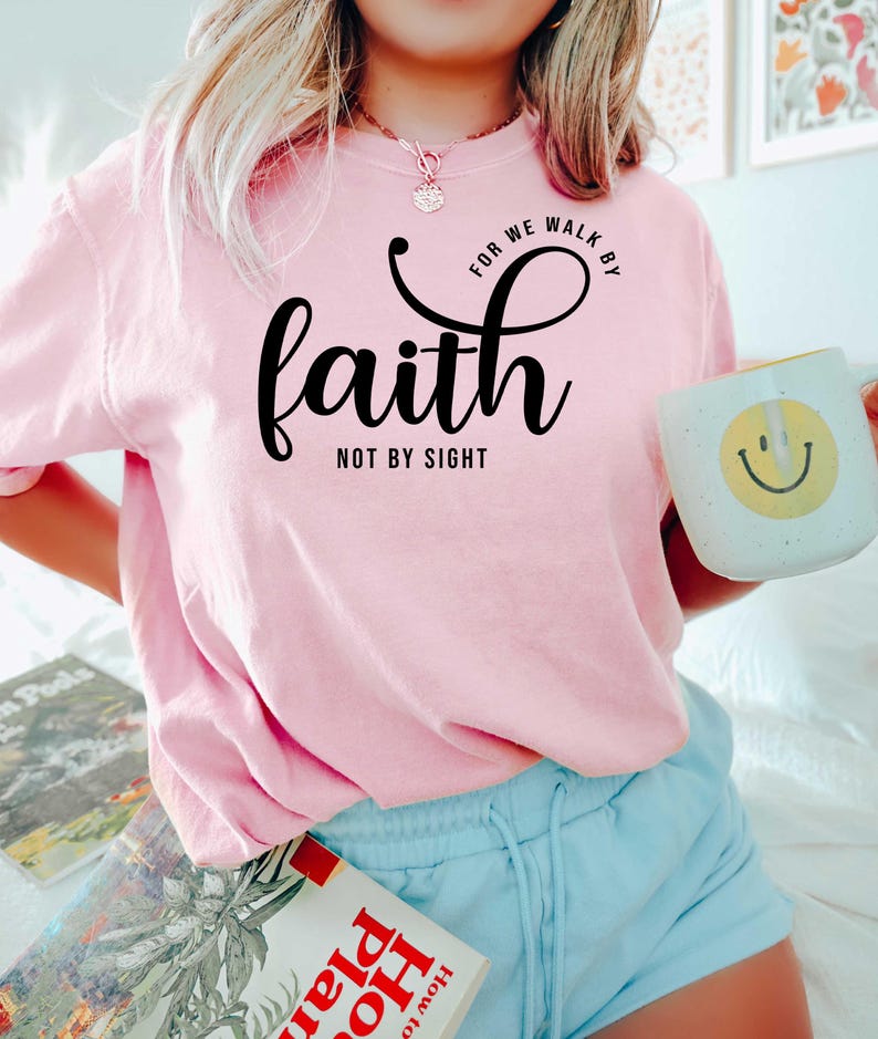Puede incluir: Camiseta rosa con el texto "For we walk by faith not by sight" en letras negras.