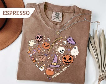 May include: Espresso-colored t-shirt with a heart-shaped Halloween design. The design includes pumpkins, ghosts, a witch's hat, and the words "Spooky Season". A silver necklace is draped across the shirt.