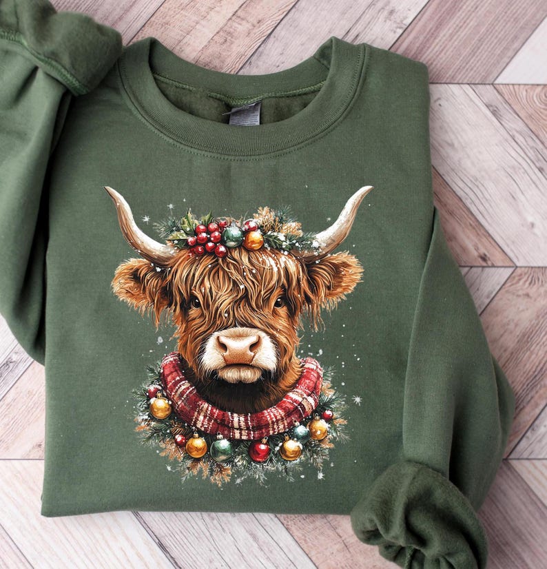 Pu&ograve; includere: Felpa verde con un'illustrazione di una mucca delle Highlands. La mucca &egrave; adornata con una ghirlanda festiva e una sciarpa a quadri, con decorazioni. Il design &egrave; centrato sulla parte anteriore della felpa, ideale per le festivit&agrave;.
