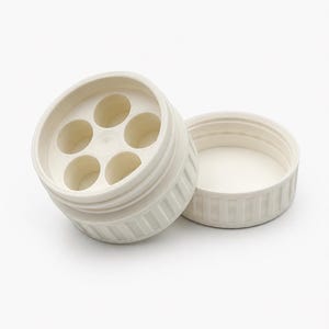 May include: Off-white plastic container with a lid. The container has a circular design with six evenly spaced holes. The lid is separate and has a ribbed texture. The container is designed to hold small items.