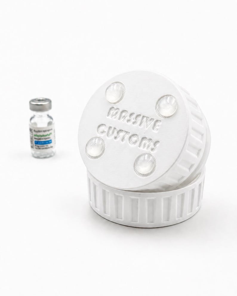 May include: A white, cylindrical product with the text "MASSIVE CUSTOMS" embossed on the top. The product has a ridged base and four clear, circular attachments. A small glass vial with a silver cap is in the background.