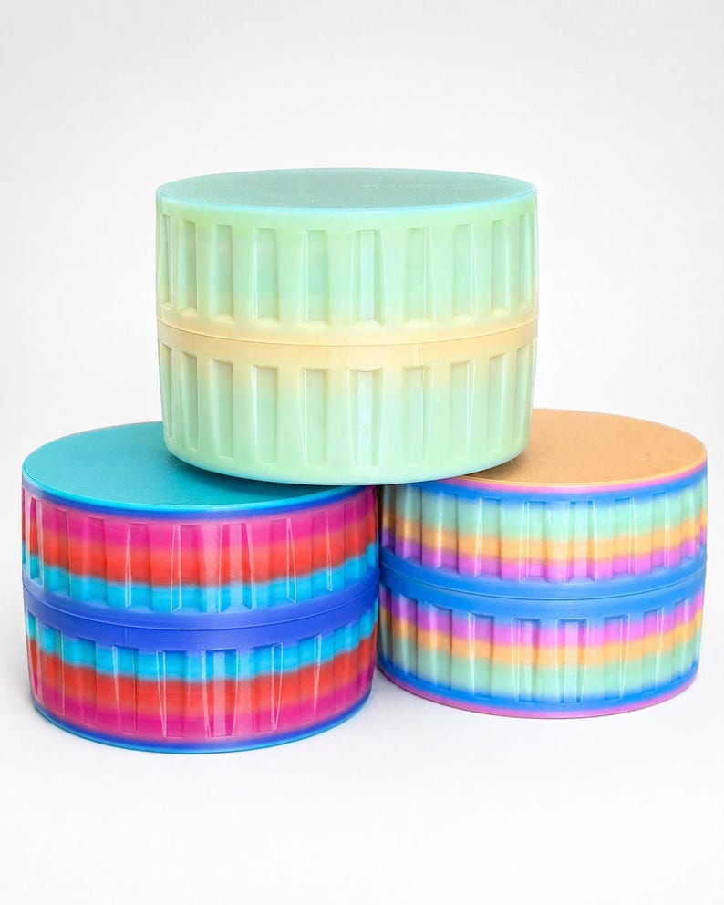 May include: Three colorful, cylindrical containers stacked on top of each other. The containers have a ribbed design and are in shades of blue, pink, orange, yellow, and green. The lids are solid colors, with a blue, green, and orange lid.