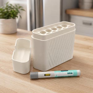 May include: A white plastic organizer with a removable tray and a compartment with multiple circular openings. A prefilled medication pen with a 0.25 mg dose is also present. The objects are on a light wood surface.