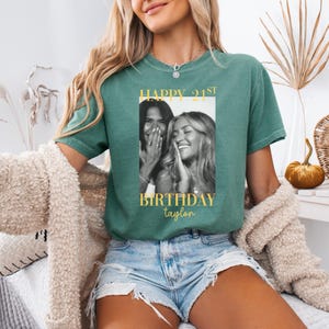 May include: Green t-shirt with a black and white photo of two laughing women. The shirt has gold text that reads "HAPPY 21ST BIRTHDAY taylor". The model is wearing denim shorts and a cream-colored cardigan.