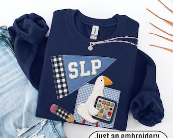 May include: A navy blue sweatshirt featuring a light blue pennant with the letters SLP, a black and white checkered pencil, and a white goose holding a colorful grid of icons. The design includes the text Just an embroidery effect print.