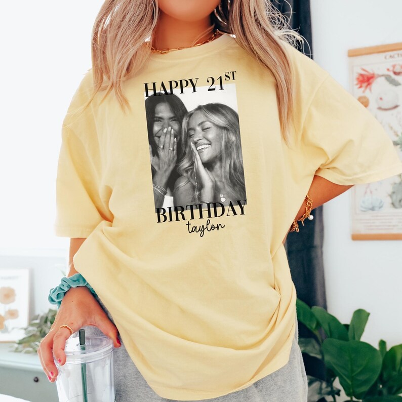 May include: A light yellow t-shirt with a black and white photo print. The print features two smiling women and the text "HAPPY 21ST BIRTHDAY taylor". The shirt is a casual style.