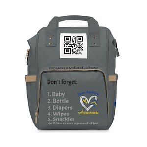 May include: Gray diaper bag backpack with a black and white QR code, the text "Downsydad.shop", and a list of items to pack: "Don't forget: 1. Baby 2. Bottle 3. Diapers 4. Wipes 5. Snackies 6. Mom on speed dial". The bag also has a yellow heart with blue and yellow ribbons and the text "Down Syndrome Awareness".