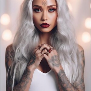 May include: A woman with long, silver hair and tattoos on her arms is wearing a white top. She has red lipstick and a decorative design on her forehead.